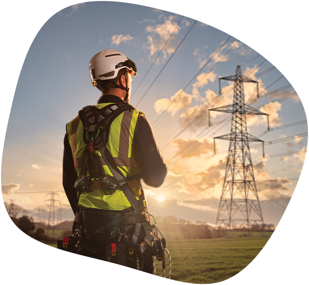 Ein ausgerüsteter Servicetechniker blickt bei Sonnenuntergang auf eine Hochspannungsleitung – Symbol für Verantwortung, Sicherheit und moderne Instandhaltung im Bereich technischer Infrastruktur.